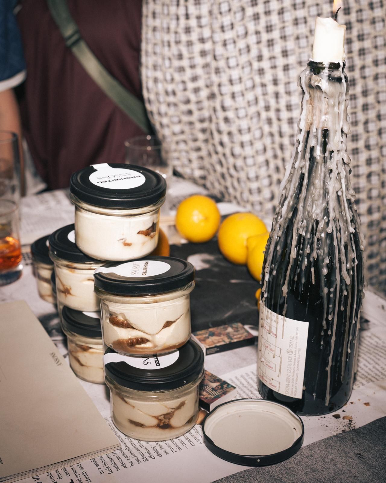 Gestapelte Tiramisù-Gläser mit personalisierten Deckel-Etiketten auf einem Event-Tisch, daneben Zitronen und eine Kerzenflasche